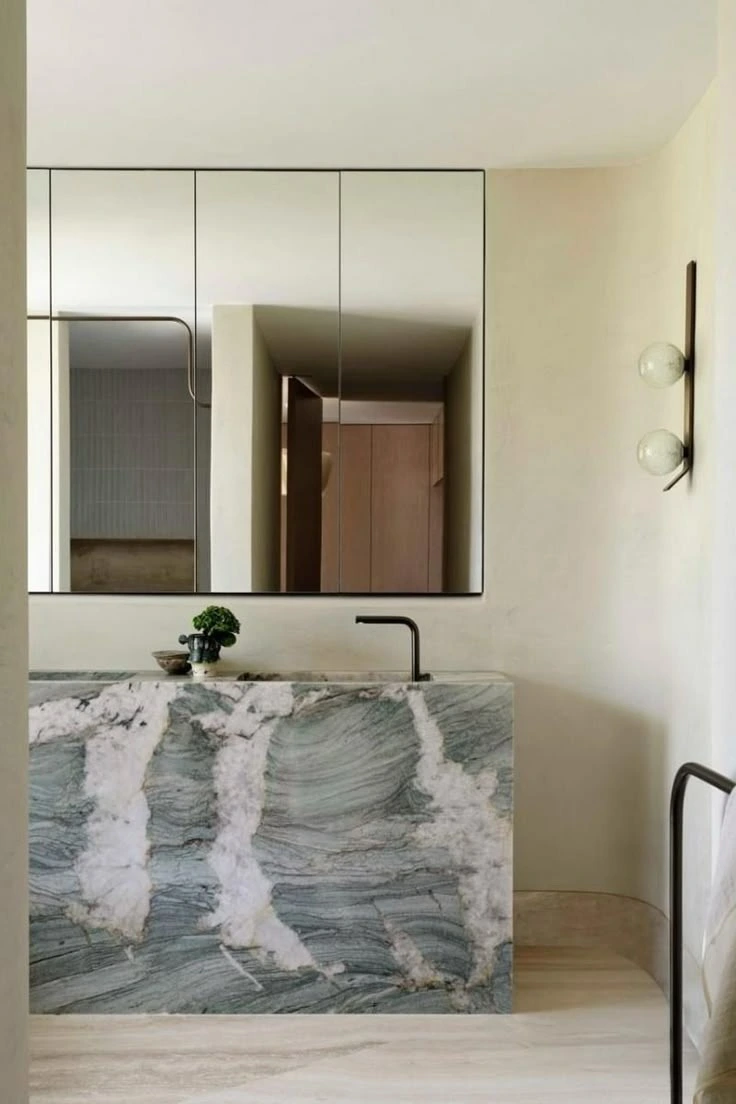 Banheiro minimalista com bancada em quartzito verde-cinza de veios brancos dramáticos, espelheira e arandelas esféricas
