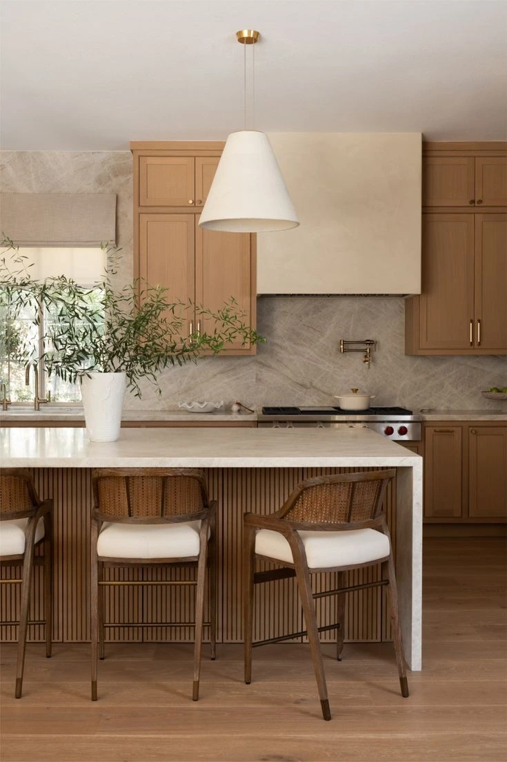 Cozinha com ilha de mármore claro, backsplash em pedra natural, marcenaria em carvalho e pendente branco